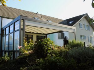 Dieser Wintergarten kann mit seinem Rolladen Sonnenschutz bieten. Wenn diese Senkrechtmarkise und das Sonnensegel geöffnet ist, kann die Luft zirkulieren.